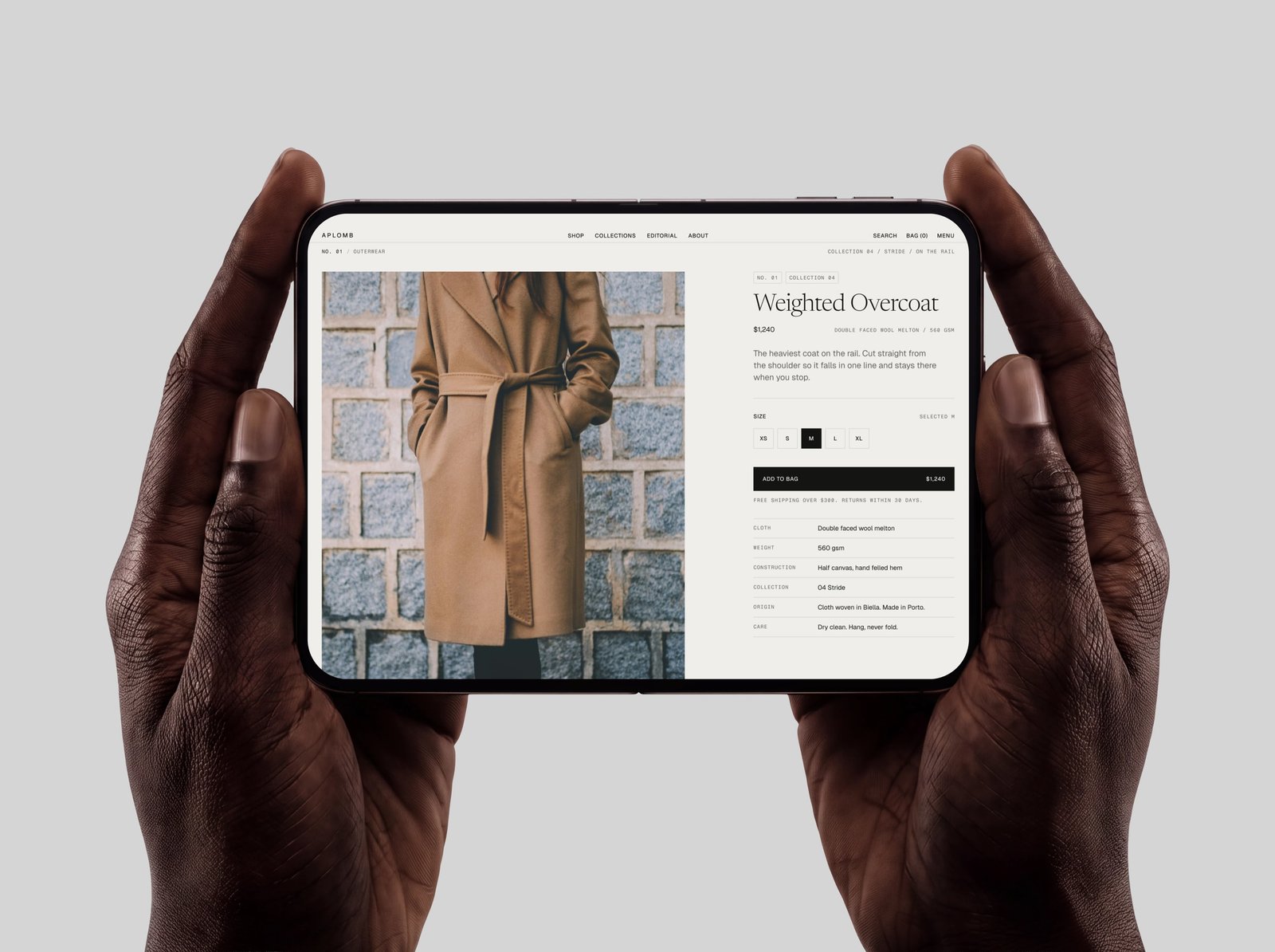 A product page held in two hands on a tablet, showing the Weighted Overcoat beside a specification table